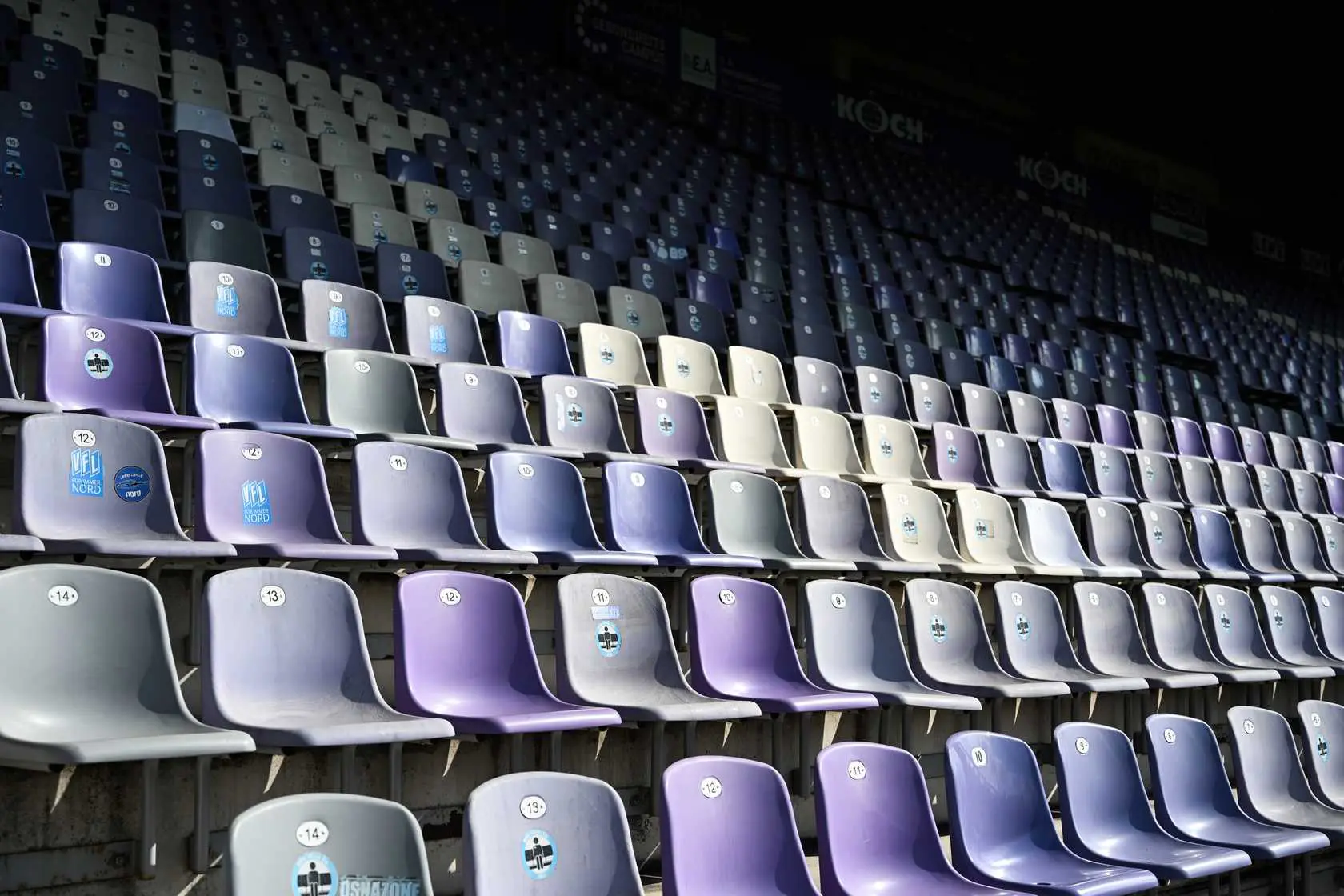 Stadion Sitze in lila und grau, mit Nummern und Logos. Leere Tribüne.