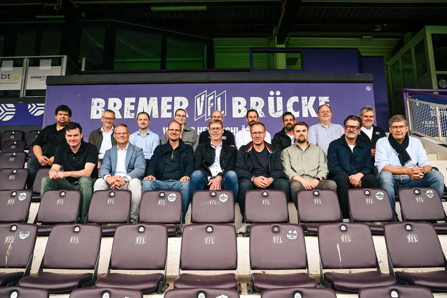 Gruppe zur Begehung Bremer Brücke sitzt auf Stadiontribüne. Planer vor Ort.