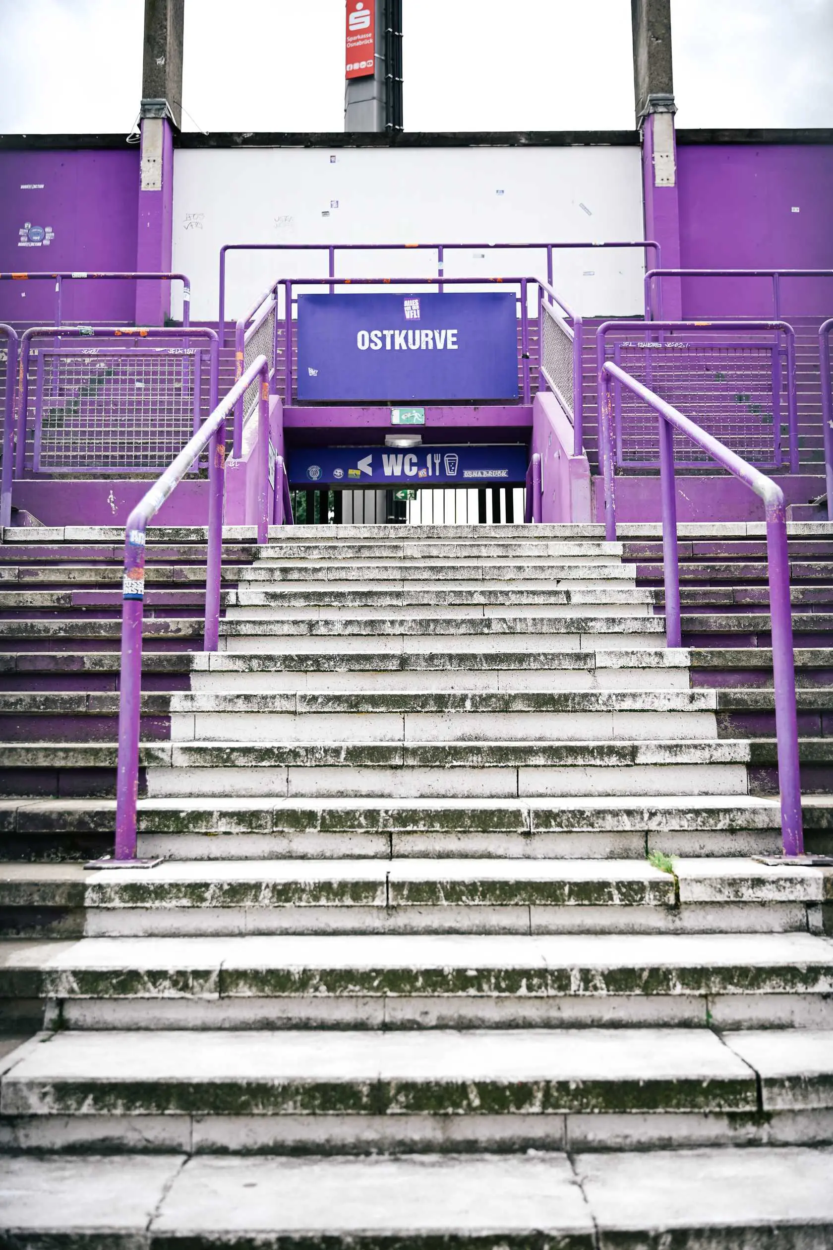 DSC_6543 Treppe zur Ostkurve, lila Geländer und Beschilderung. WC-Symbol sichtbar.