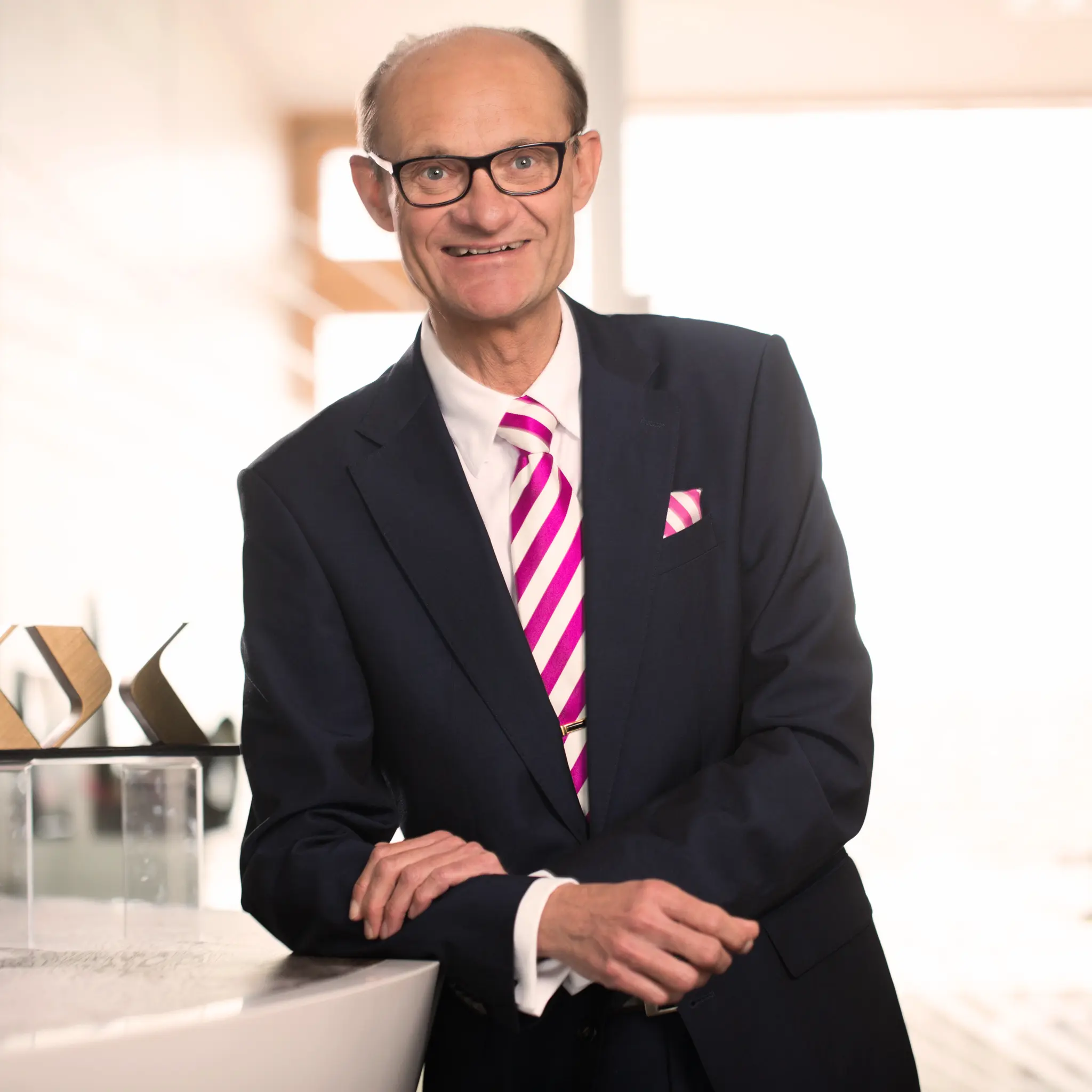 Michael Koch im Anzug mit pinkfarbener Krawatte und Brille.